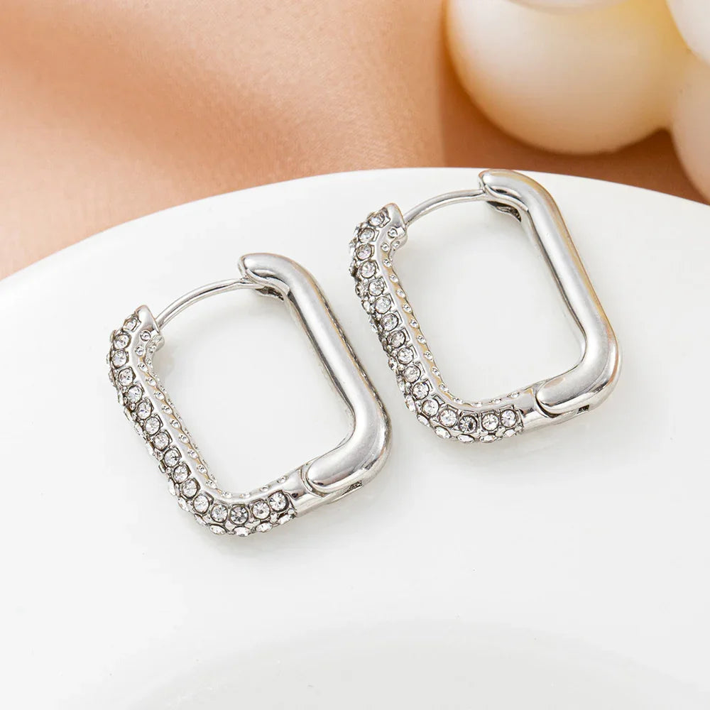 Silver square hoop earrings with clear crystal accents on a white plate