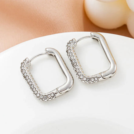 Silver square hoop earrings with clear crystal accents on a white plate
