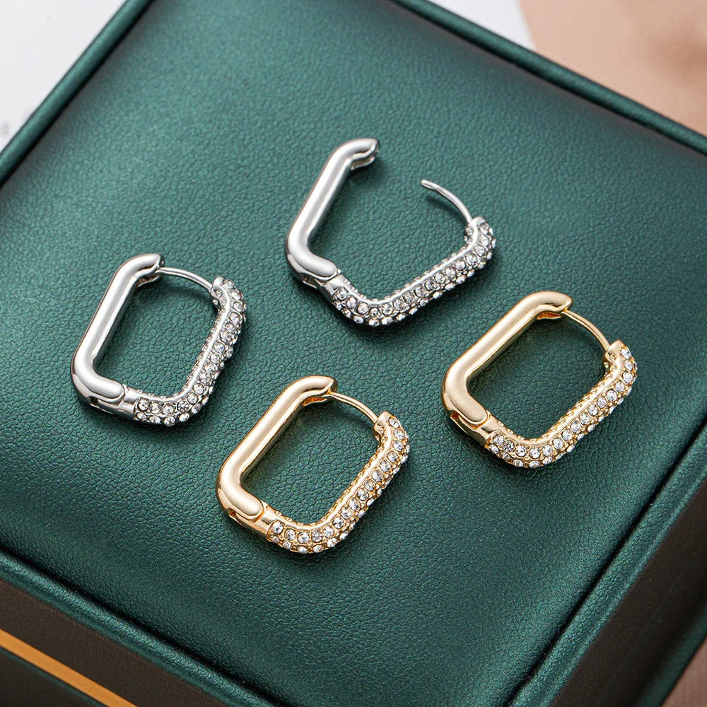 Square hoop earrings in gold and silver tones with sparkling crystals on green box