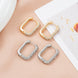 Gold and silver rectangular hoop earrings with pave crystals on a satin background