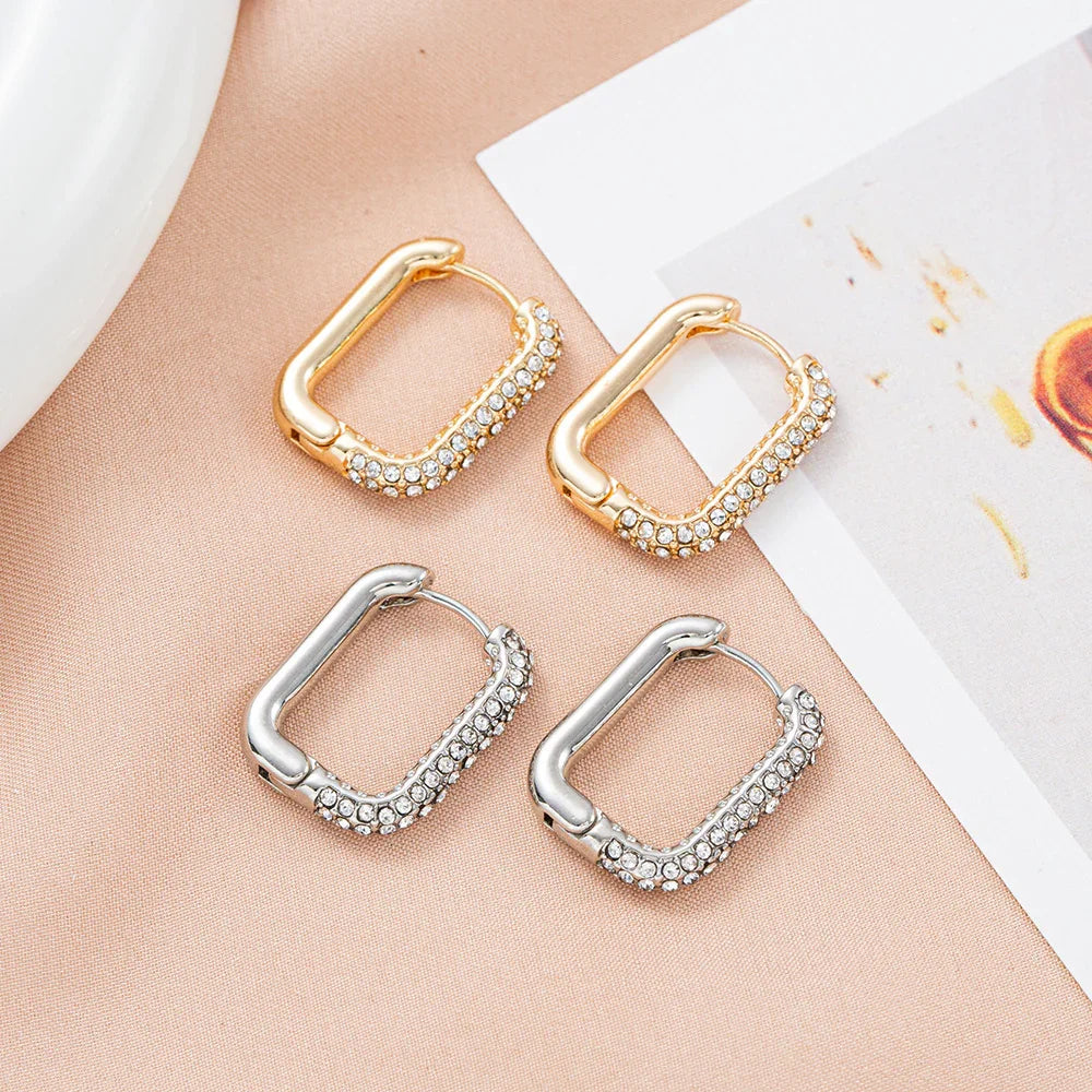 Gold and silver rectangular hoop earrings with pave crystals on a satin background