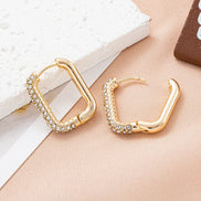Gold geometric hoop earrings with crystal accents on a soft beige fabric background